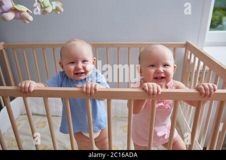 Les enfants jumeaux, garçon et fille, sourient en se tenant debout le berceau Banque D'Images