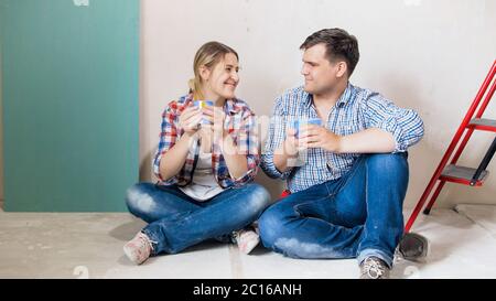 Un couple souriant et heureux assis sur le sol et buvant du café pendant la pause dans la rénovation de la maison Banque D'Images