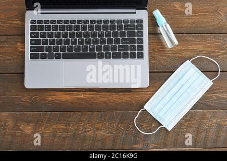 Vue de dessus vers le bas sur ordinateur portable, masque et désinfectant pour les mains sur fond en bois foncé, quarantaine bureau à domicile, espace de copie Banque D'Images