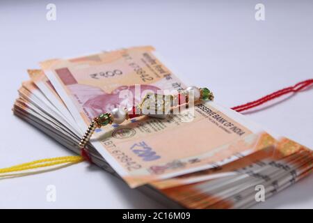 Raksha Bandhan concept de festival montrant le designer Rakhi ou Wrist Band Avec du riz et du kumkum épars, placés avec de la monnaie indienne sur coloré Banque D'Images