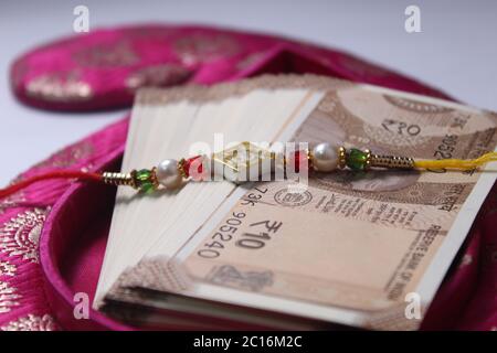 Raksha Bandhan concept de festival montrant le designer Rakhi ou Wrist Band Avec du riz et du kumkum épars, placés avec de la monnaie indienne sur coloré Banque D'Images
