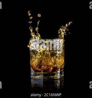 Verre de whisky éclaboussant ou autre alcool avec cube de glace isolé sur fond noir Banque D'Images