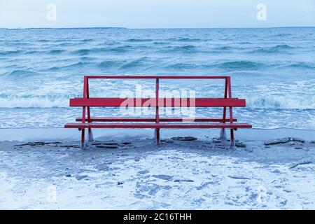 Banc rouge recouvert de glace est frappé par la mer d'hiver. Vagues glaciales de la mer Baltique sur une plage vide. Banque D'Images