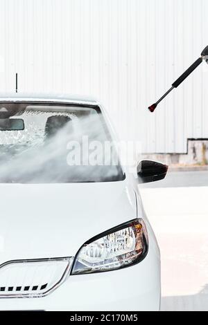 Un lavage de voiture blanc avec de l'eau sous pression au service de lavage libre à l'extérieur par temps ensoleillé. Concept de lavage manuel de voiture. Banque D'Images