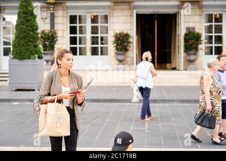 Une femme avec un sac de courses regarde son téléphone devant l'InterContinental Grand Hotel de Bordeaux, un grand hôtel, Bordeaux, France Banque D'Images