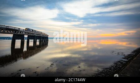 Train traversant un estuaire calme de Tay au coucher du soleil, Dundee, Écosse, Royaume-Uni. Banque D'Images