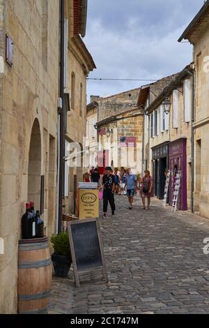 Rue piétonne pavée à Saint-Emilion avec un tonneau de vin, un tableau noir et des touristes qui passent, France Banque D'Images