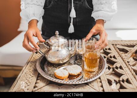 Femme mains servant une cérémonie traditionnelle marocaine de thé à la menthe avec des biscuits et thé argent vintage. Hospitalité et service au Maroc, Marrakech. Banque D'Images