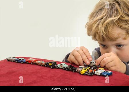 QUEENSTOWN, AFRIQUE DU SUD - 17 2015 MAI - petit garçon blond jouant avec des voitures de jouets vintage sur du velours rouge Banque D'Images