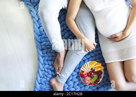 Jeune homme et femme enceinte assis avec une assiette de fruits Banque D'Images