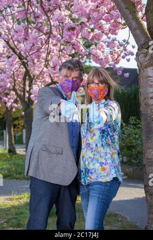 Couple senior en tissu coloré masques et gants jetables comme protection contre la propagation du coronavirus donnant un pouce vers le haut pour montrer qu'ils Banque D'Images