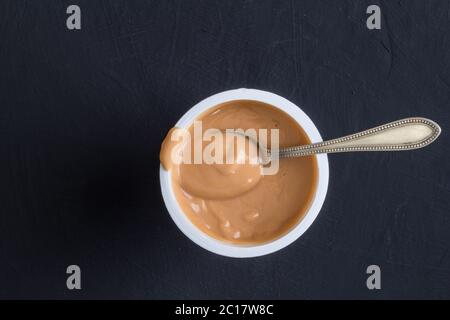 Fond de yaourt vue du dessus prise de yaourt au caramel dans une tasse en plastique avec une petite cuillère en argent Banque D'Images