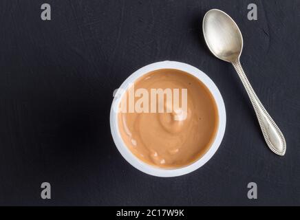 Fond de yaourt vue du dessus prise de yaourt au caramel dans une tasse en plastique avec une petite cuillère en argent Banque D'Images