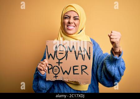 Jeune femme arabe magnifique portant le hijab islamique tenant la bannière avec les femmes message de puissance agacé et frustré criant avec colère, fou et hurlant Banque D'Images