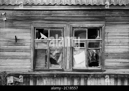Photo noir et blanc vieux village en bois abandonné maison avec verre brisé dans les fenêtres, Russie. Banque D'Images