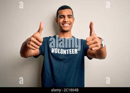 Jeune homme afro-américain élégant portant un t-shirt avec message de volontaire approuvant faire un geste positif à la main, pouces vers le haut souriant Banque D'Images