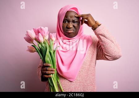 Jeune afro-américaine de taille plus, portant le hijab musulman tenant un bouquet de tulipes roses inquiet et stressé à propos d'un problème de main sur le front, Banque D'Images