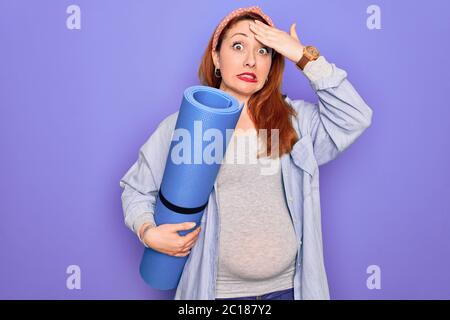 Jeune belle redhead femme enceinte s'attendant à bébé tenant tapis à faire l'exercice prénatal stressé avec la main sur la tête, choqué avec honte et surprise Banque D'Images