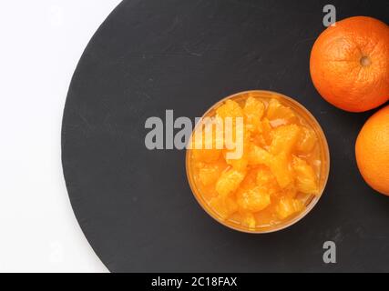 Tranches d'orange dans un bol à pudding sur ardoise ronde noire avec deux oranges entières sur le côté. Vue de dessus de la nourriture Banque D'Images