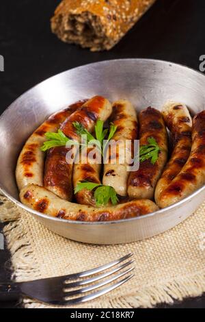 Saucisses frites avec persil, pain et fourchette dans une casserole sur fond noir Banque D'Images