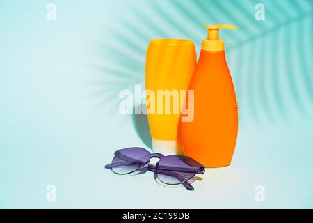 Contenants orange sans étiquette pour lotion, lunettes de soleil violettes sur fond bleu, espace pour le texte Banque D'Images