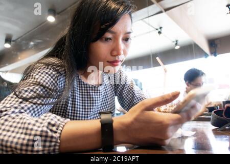Une jeune femme assise dans un restaurant et regardant dans son téléphone mobile. Banque D'Images