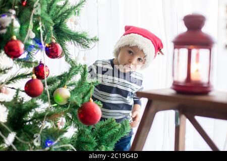 Beau garçon blond, décorant l'arbre de noël avec des boules et des cordes légères à la maison Banque D'Images