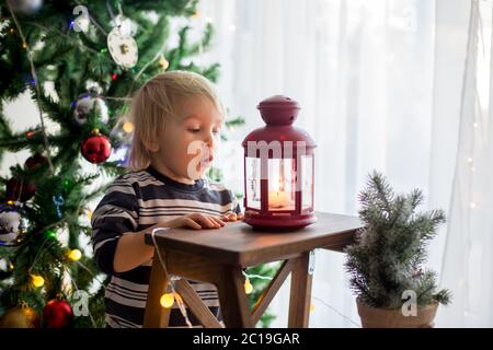 Beau garçon blond, décorant l'arbre de noël avec des boules et des cordes légères à la maison Banque D'Images