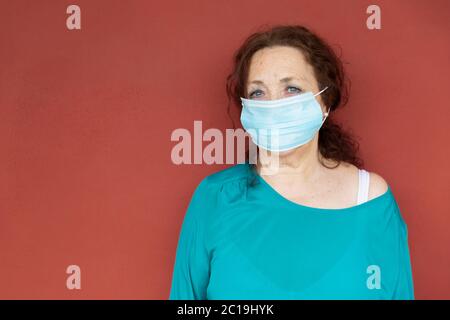 Portrait de la vieille femme avec masque protecteur sur le mur rouge. Confinement par coronavirus. Concept Covid-19. Banque D'Images