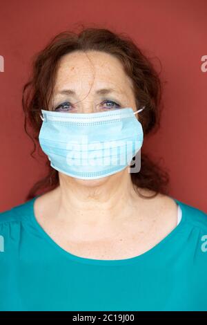 Portrait de la vieille femme avec masque protecteur sur le mur rouge. Confinement par coronavirus. Concept Covid-19. Banque D'Images