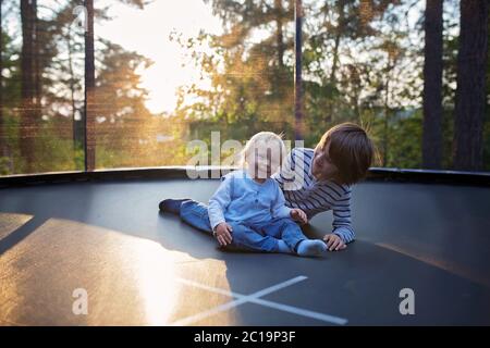 Un petit garçon de la préadolescence et son petit frère sautant sur le trampoline. Des enfants heureux sautant au coucher du soleil, faisant différentes formes Banque D'Images