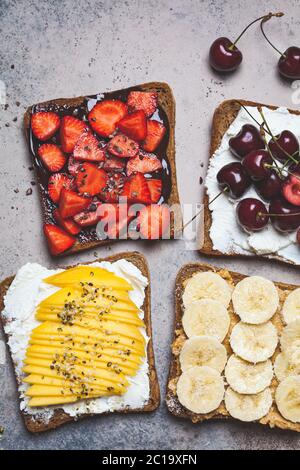 Différents toasts de fruits doux avec banane, mangue, cerise et fraises sur fond sombre. Banque D'Images