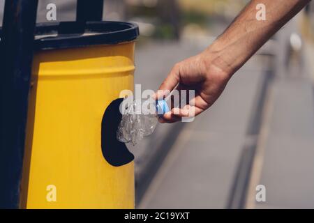 Attention sélective sur la main de déposer la bouteille de plastique vide dans le bac à déchets jaune. Banque D'Images