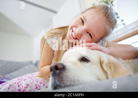 Une fillette se câlin avec un chien de retriever doré sur le canapé à la maison Banque D'Images