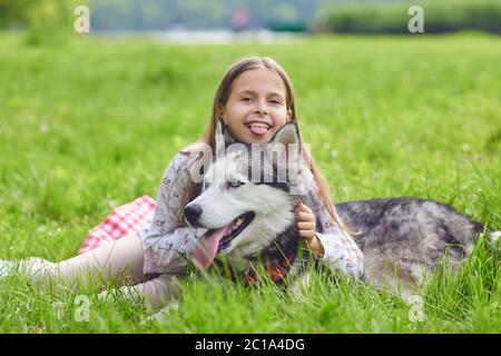 Une jeune fille souriante encroise un chien husky allongé sur de l'herbe verte sur la nature estivale. Banque D'Images