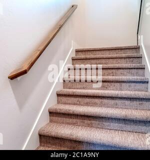 Escalier intérieur de la maison recouvert de moquette à cadre carré avec main courante marron contre le mur latéral blanc Banque D'Images