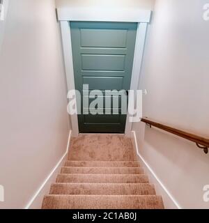 Escalier intérieur carré de la maison avec des bandes de roulement recouvertes de moquette qui mène à la porte du sous-sol Banque D'Images