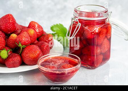 Confiture de fraises dans un pot en verre à côté des fraises fraîches. Sur fond gris. Blancs de fruits d'hiver faits maison. Mise au point sélective. Copier l'espace Banque D'Images