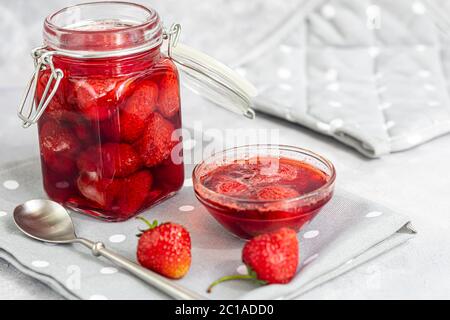 Confiture de fraises dans un pot en verre à côté des fraises fraîches. Sur fond gris. Blancs de fruits d'hiver faits maison. Mise au point sélective. Copier l'espace Banque D'Images