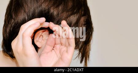 Potins, rumeurs, murmure, concept d'audition. Jeune femme mettant l'oreille de la main pour entendre mieux. Studio tourné sur fond gris. Gros plan, espace de copie Banque D'Images