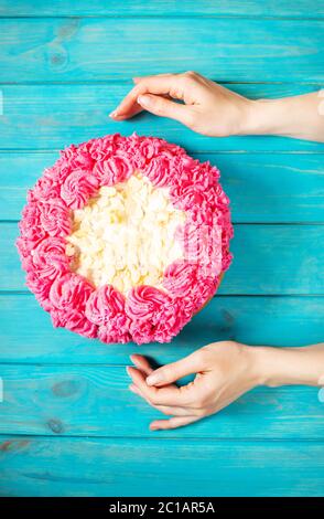 Woman's hands couper le gâteau avec la crème rose sur fond de bois bleu. Gâteau rose. Vue d'en haut Banque D'Images