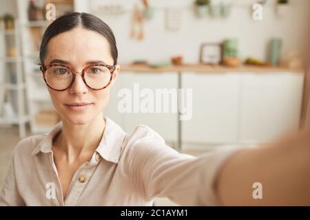 Portrait ton chaud de la jeune femme en réglant l'appareil photo selfie tout en se tenant dans un intérieur confortable, espace de copie Banque D'Images