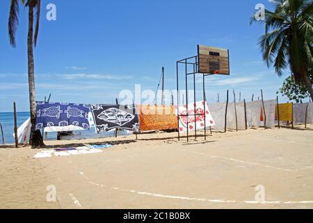 Nappes à vendre suspendues à la vente devant le terrain de basket-ball sur la plage avec des bateaux, village d'Ampangorinana, île de Nosy Komba, Madagascar. Banque D'Images