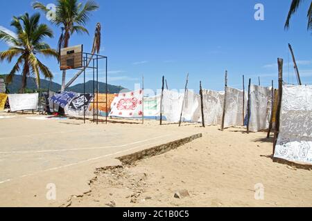 Nappes à vendre suspendues à la vente devant le terrain de basket-ball sur la plage avec des bateaux, village d'Ampangorinana, île de Nosy Komba, Madagascar. Banque D'Images