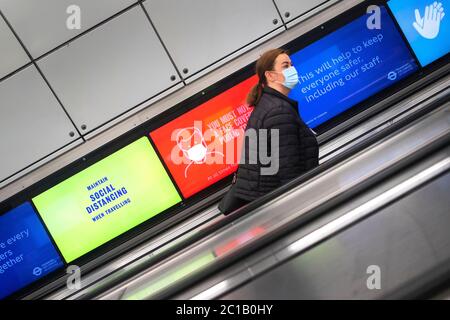 Un passager portant un masque facial passe des écrans d'information sur la distance sociale sur un escalier mécanique à la station de métro Tottenham court Road à Londres, car les magasins non essentiels en Angleterre ouvrent leurs portes aux clients pour la première fois depuis que des restrictions de verrouillage du coronavirus ont été imposées en mars. Banque D'Images