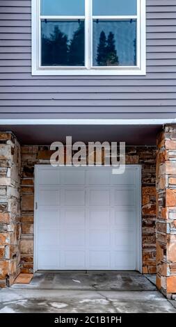 Récolte verticale porte de garage blanche lambrissée de la maison avec parement gris et mur extérieur en pierre Banque D'Images
