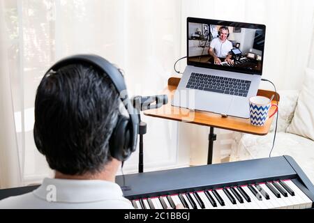 Professeur de piano masculin donnant des leçons de piano en ligne à la maison à l'aide d'un ordinateur portable. Banque D'Images