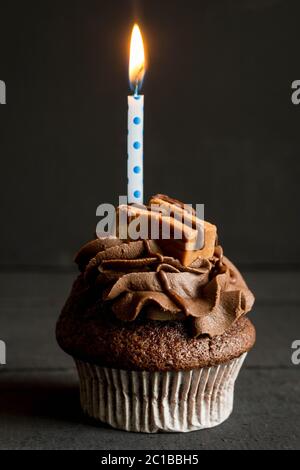 Tasse de chocolat gâteau décoré avec glaçage buttercream et fudge carrés avec bougie allumée sur fond noir Banque D'Images