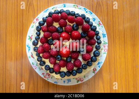 Un gâteau décoré de glaçage au beurre et de fruits d'été, dont des fraises, des framboises et des bleuets. Banque D'Images