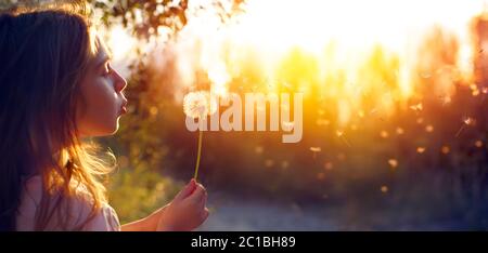 Petite fille soufflant Dandelion Flower au coucher du soleil - arrière-plan défoqué Banque D'Images